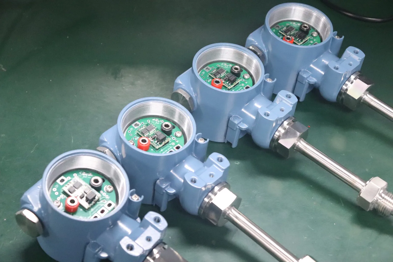 Four SEGMENsensor pressure transmitters with opened housings and stainless steel process connections during assembly, before overload testing and calibration